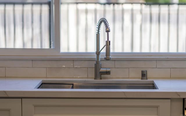 room details with tasteful backsplash, white cabinetry, a sink, and light stone counters