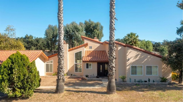 back of property featuring a tiled roof, a chimney, and stucco siding