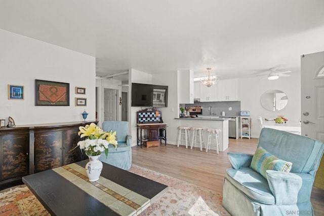 living room with light wood-type flooring, ceiling fan with notable chandelier, and sink