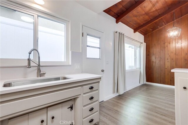 kitchen with sink, vaulted ceiling with beams, white cabinetry, wood ceiling, and light hardwood / wood-style floors