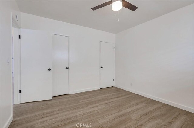 unfurnished bedroom featuring ceiling fan, light hardwood / wood-style floors, and two closets