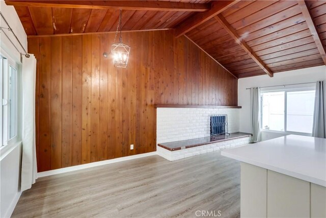 unfurnished living room featuring vaulted ceiling with beams, wooden ceiling, wooden walls, and light hardwood / wood-style flooring