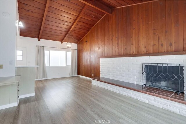 unfurnished living room with wood walls, lofted ceiling with beams, wooden ceiling, hardwood / wood-style flooring, and a fireplace