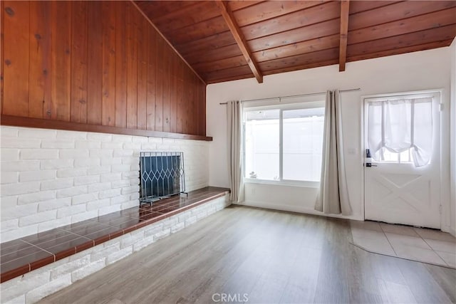 unfurnished living room featuring vaulted ceiling with beams, wood ceiling, wooden walls, a fireplace, and light hardwood / wood-style floors