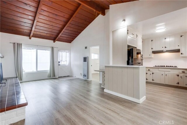 kitchen with white cabinetry, black fridge, light wood-type flooring, gas cooktop, and beam ceiling