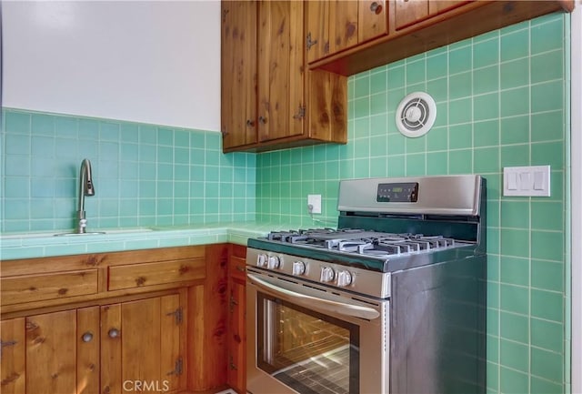 kitchen featuring sink, stainless steel range with gas stovetop, tile countertops, and decorative backsplash