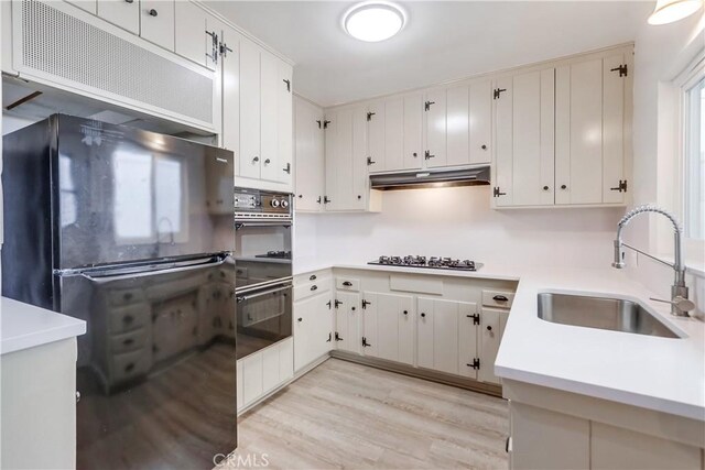 kitchen with sink, black appliances, white cabinets, and light wood-type flooring