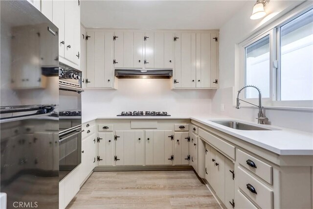 kitchen featuring sink, gas cooktop, white cabinetry, black double oven, and light wood-type flooring