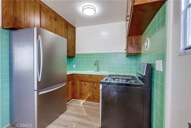 kitchen with tasteful backsplash, sink, light hardwood / wood-style floors, and appliances with stainless steel finishes