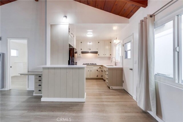 kitchen featuring sink, vaulted ceiling with beams, black cooktop, light wood-type flooring, and white cabinets