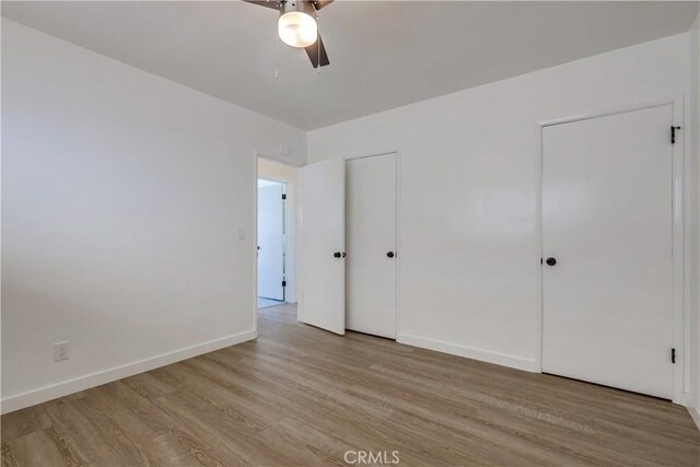 unfurnished bedroom featuring two closets, ceiling fan, and light wood-type flooring