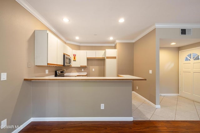 kitchen featuring white cabinets, appliances with stainless steel finishes, kitchen peninsula, ornamental molding, and light tile patterned flooring