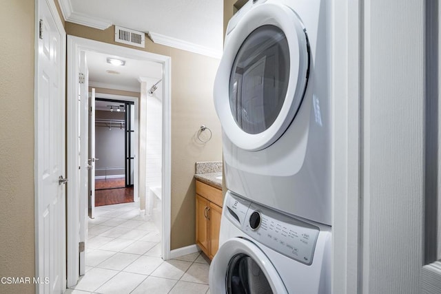 clothes washing area featuring crown molding, stacked washing maching and dryer, and light tile patterned flooring