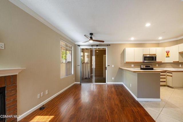 kitchen with ceiling fan, a brick fireplace, kitchen peninsula, crown molding, and white cabinetry