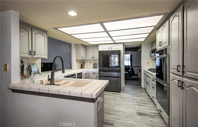 kitchen with kitchen peninsula, light hardwood / wood-style flooring, tile countertops, refrigerator, and decorative backsplash