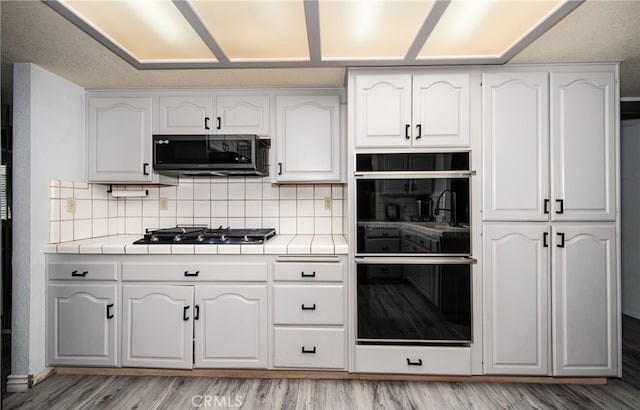 kitchen with light hardwood / wood-style floors, tile counters, tasteful backsplash, and white cabinetry