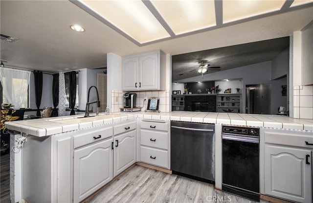 kitchen with white cabinets, kitchen peninsula, tile counters, and light wood-type flooring