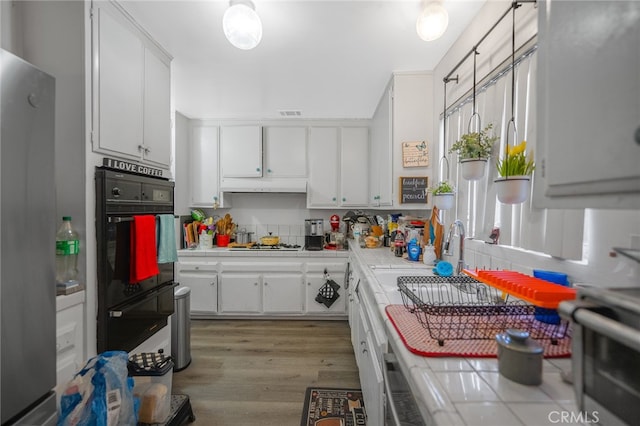 kitchen featuring appliances with stainless steel finishes, tasteful backsplash, white cabinets, tile countertops, and light wood-type flooring