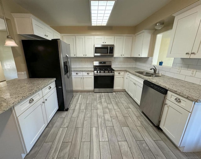 kitchen with white cabinets, appliances with stainless steel finishes, pendant lighting, light hardwood / wood-style floors, and light stone counters