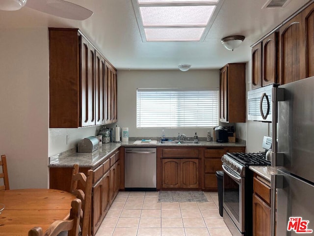 kitchen featuring light tile patterned flooring, sink, a skylight, and stainless steel appliances