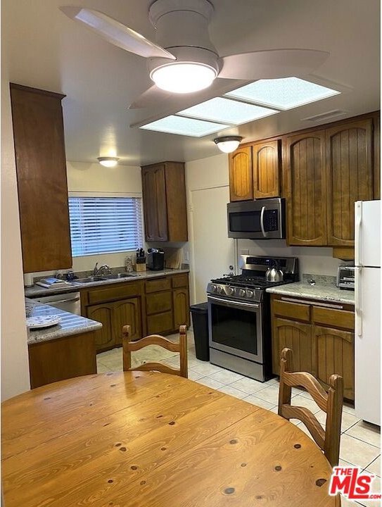 kitchen featuring a skylight, appliances with stainless steel finishes, light tile patterned floors, and sink