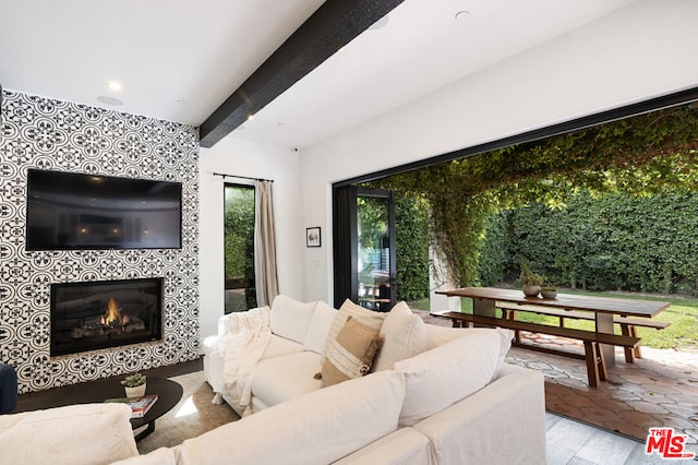 living room with beam ceiling, a tiled fireplace, and light hardwood / wood-style flooring