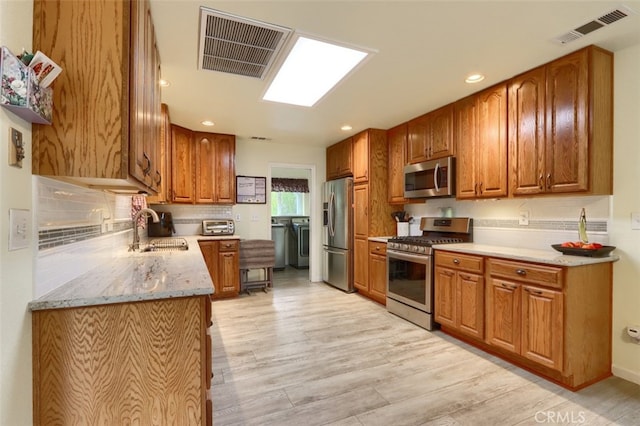 kitchen with light wood-type flooring, light stone counters, sink, backsplash, and appliances with stainless steel finishes