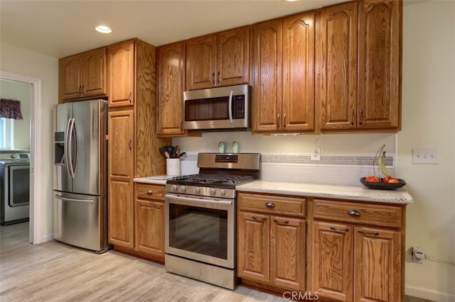 kitchen with washer / clothes dryer, stainless steel appliances, light hardwood / wood-style floors, and decorative backsplash