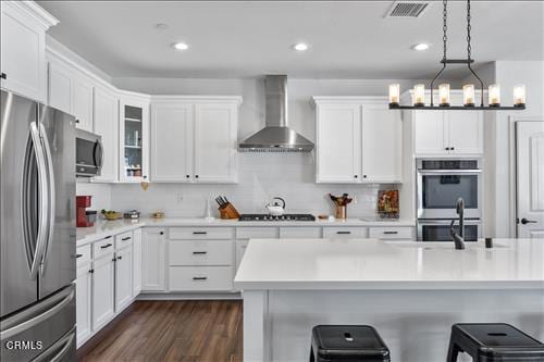 kitchen featuring dark wood-type flooring, a notable chandelier, hanging light fixtures, wall chimney exhaust hood, and stainless steel appliances