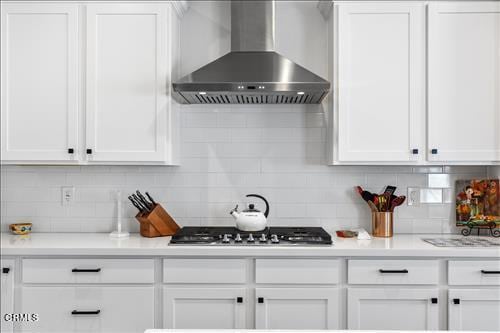 kitchen with stainless steel gas stovetop, decorative backsplash, white cabinetry, and wall chimney range hood