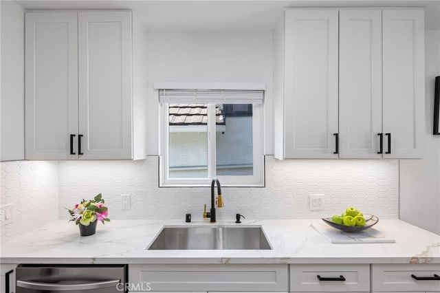 kitchen with sink, tasteful backsplash, light stone counters, stainless steel dishwasher, and white cabinets