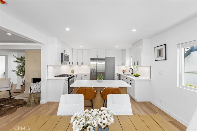 kitchen with decorative backsplash, light wood-type flooring, stainless steel appliances, a center island, and white cabinetry