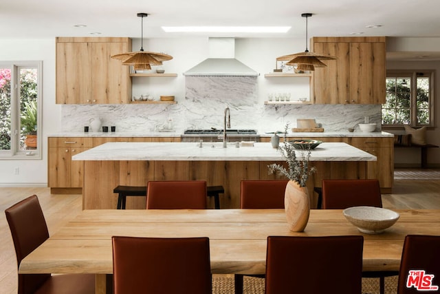 kitchen featuring a wealth of natural light, wall chimney exhaust hood, and decorative light fixtures