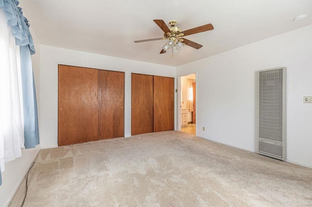 unfurnished bedroom featuring ceiling fan, light colored carpet, and multiple closets