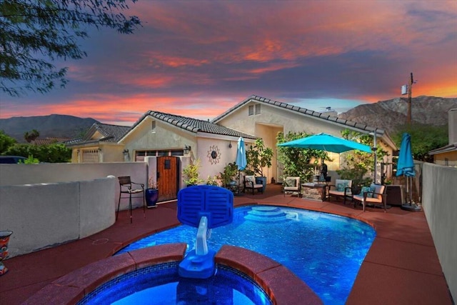 pool at dusk with a mountain view, an in ground hot tub, and a patio area