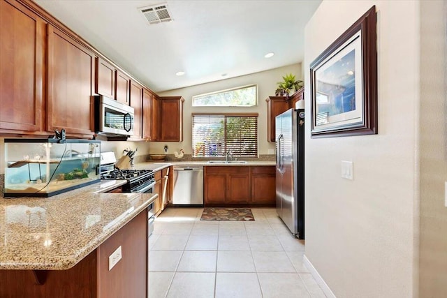 kitchen featuring light stone countertops, kitchen peninsula, vaulted ceiling, light tile patterned flooring, and appliances with stainless steel finishes