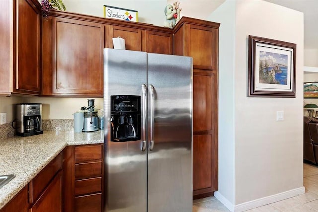 kitchen featuring light stone countertops, light tile patterned flooring, and stainless steel refrigerator with ice dispenser