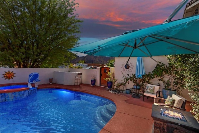 pool at dusk featuring an in ground hot tub, a patio, and a fire pit