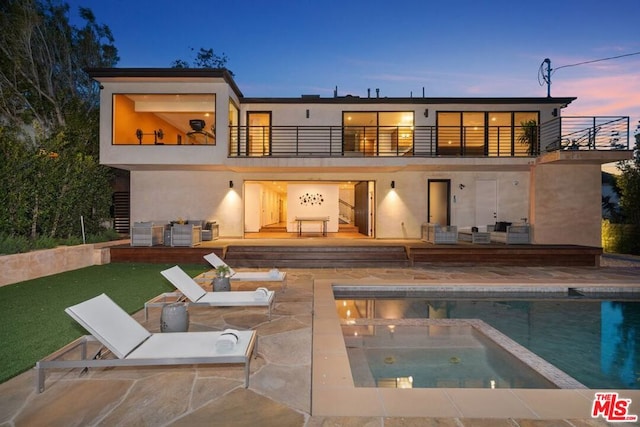 back house at dusk with a pool with hot tub, a balcony, a yard, and a patio