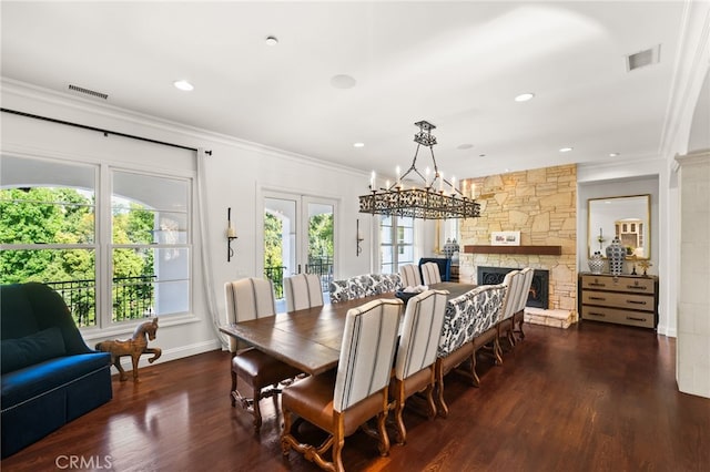 dining area with crown molding, a stone fireplace, dark hardwood / wood-style flooring, and an inviting chandelier