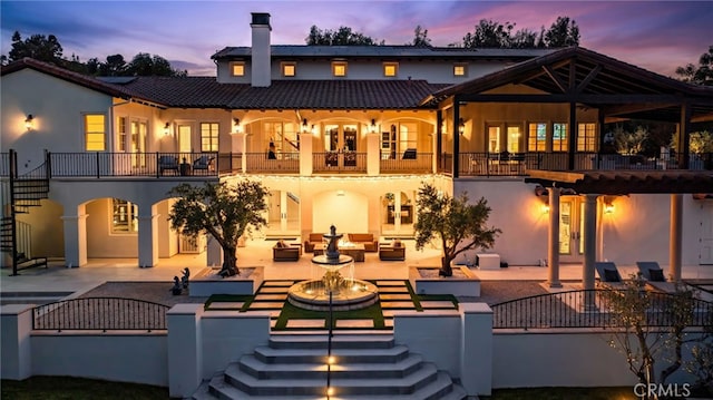 back house at dusk with a balcony, an outdoor hangout area, and a patio