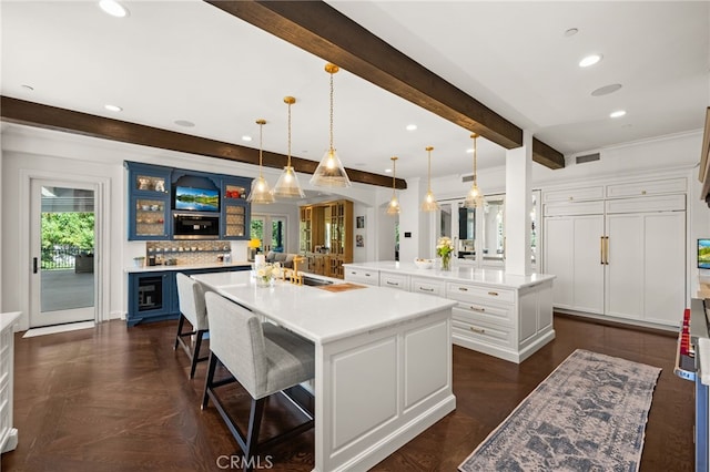 kitchen with a breakfast bar area, white cabinetry, hanging light fixtures, and a large island with sink