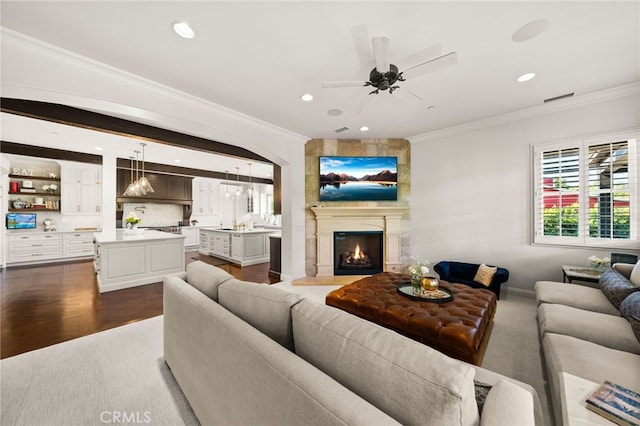 living room with ornamental molding, dark wood-type flooring, a fireplace, and ceiling fan