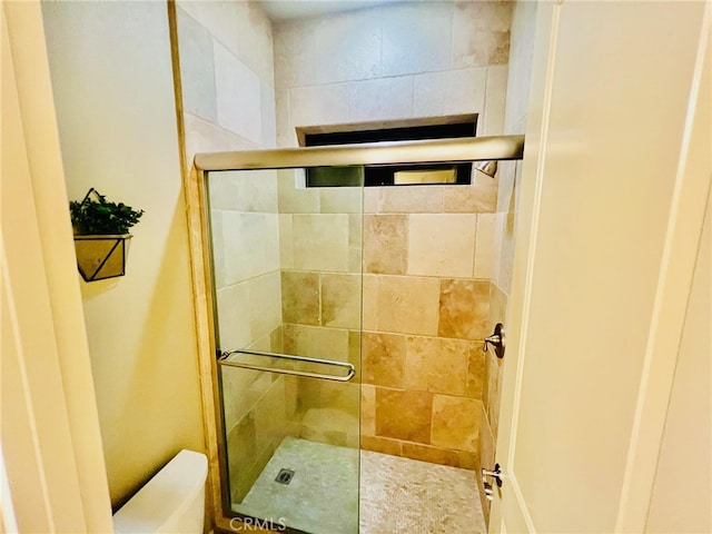 bathroom featuring a shower with door and toilet