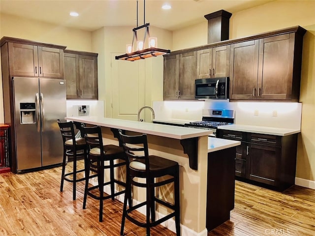 kitchen with dark brown cabinets, stainless steel appliances, light hardwood / wood-style floors, and a kitchen island with sink