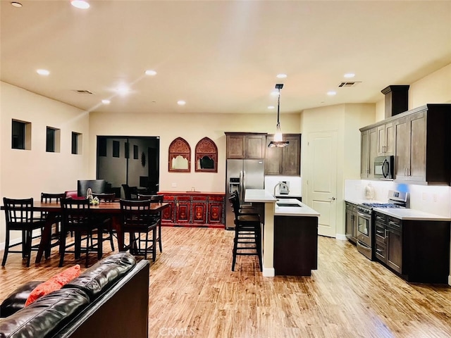 kitchen with pendant lighting, an island with sink, light hardwood / wood-style flooring, stainless steel appliances, and a kitchen bar