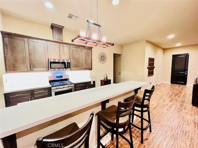 kitchen featuring dark brown cabinets, decorative light fixtures, light hardwood / wood-style flooring, stainless steel appliances, and a kitchen breakfast bar