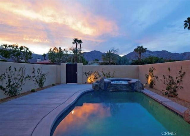 pool at dusk with a mountain view, a patio, and an in ground hot tub