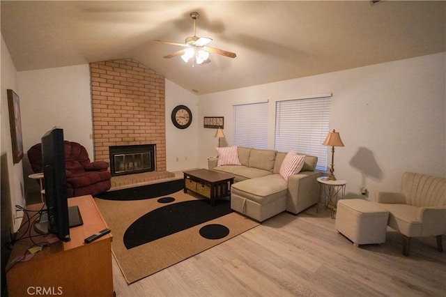 living area featuring vaulted ceiling, a brick fireplace, wood finished floors, and ceiling fan