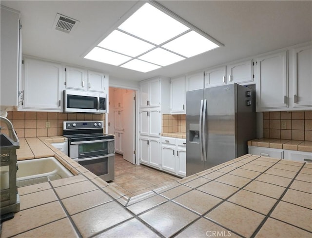 kitchen with tile counters, white cabinets, backsplash, and stainless steel appliances